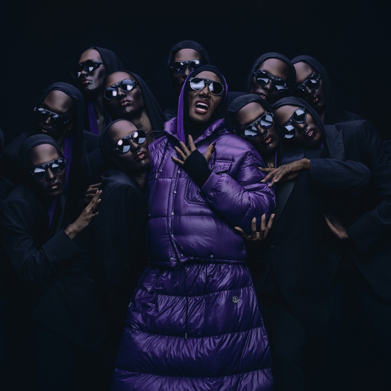 Moncler Re/Icons 2026, Pioneers in Moncler : Grace Jones en doudoune violette parmi des silhouettes en costumes sombres.