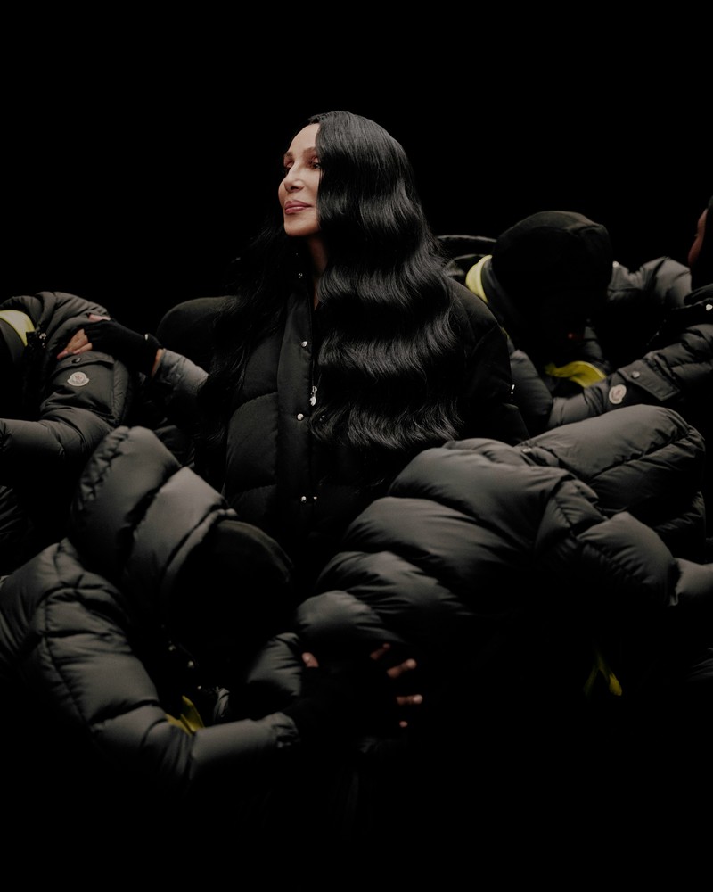 Moncler Re/Icons 2026, Cher in a black Verone down jacket, surrounded by figures in black down jackets. 