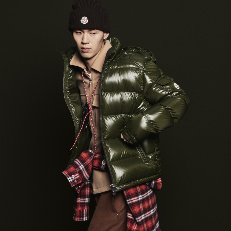Outerwear Moncler hombre. Plumífero verde brillante, camisa a cuadros, chaqueta beige, gorro con logo y pantalón marrones. 