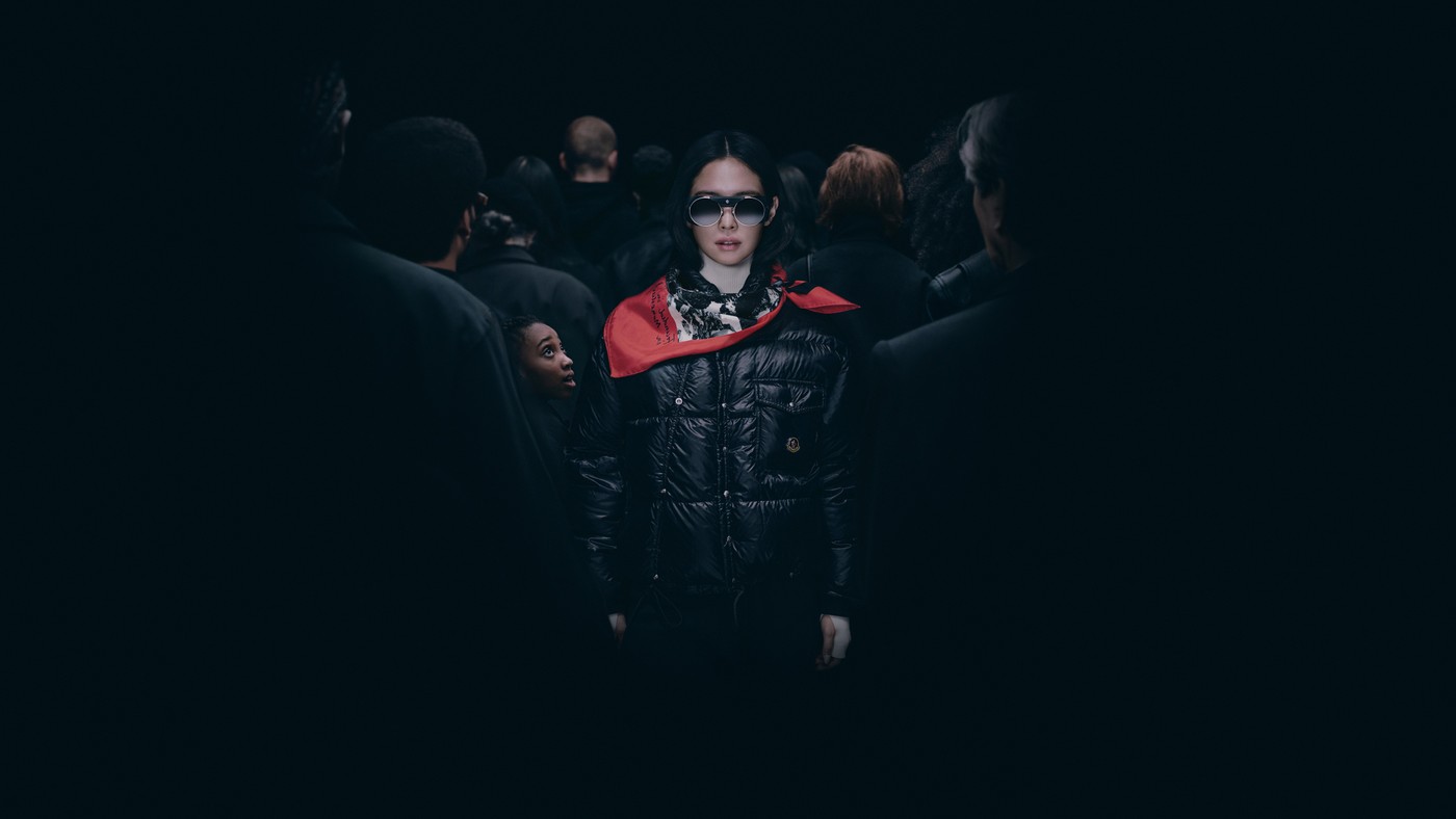 JENNIE in a black Moncler puffer and red scarf standing amid a crowd dressed in black