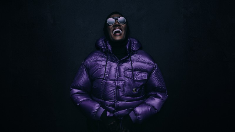 Moncler Re/Icons 2026, Grace Jones laughing in round sunglasses and a glossy purple down jacket. 
