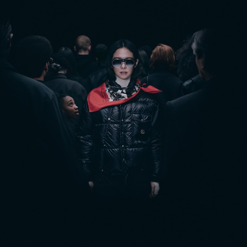 Moncler Re/Icons 2026, Pioneers in Moncler: Jennie in schwarzer Daunenjacke und rotem Tuch in einer Menge in Schwarz.