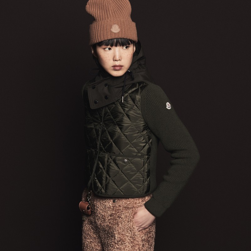 Moncler ウィメンズ。ブラウンのニット帽、フード付きダークグリーンのライトジャケットと柄パンツ。 