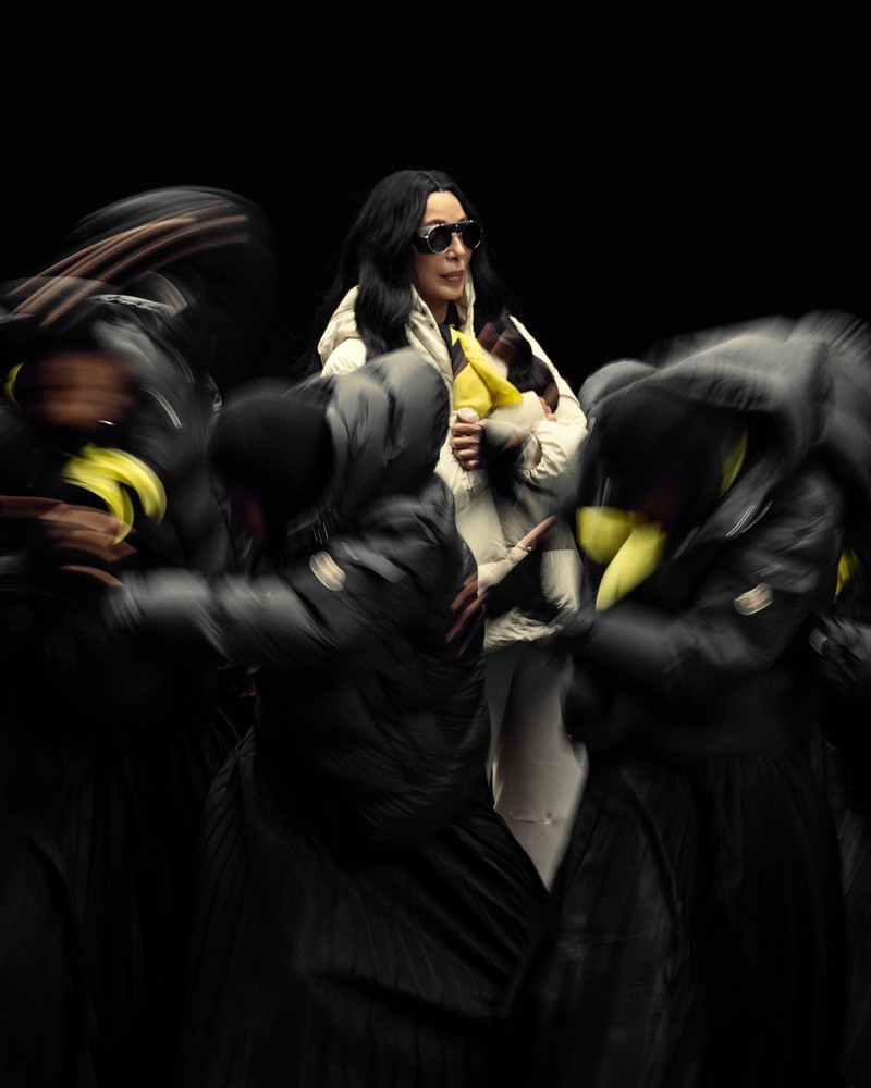 Moncler Re/Icons 2026, Cher in a cream Himalaya short down jacket with yellow scarf and the jacket displayed on the right. 
