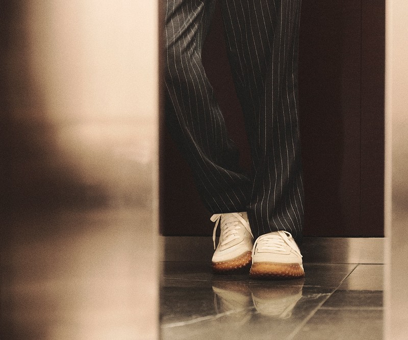 Moncler CityTrek: white and beige sneakers with brown rubber, black pinstripe trousers.