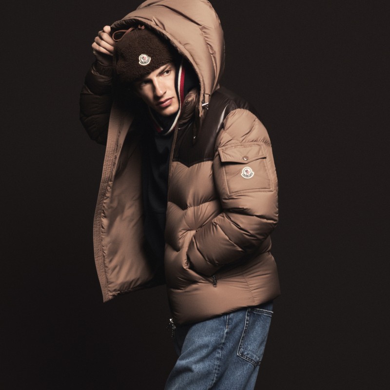 Moncler outerwear for men. Camel hooded down jacket with glossy brown patch, brown shearling hat and blue jeans. 