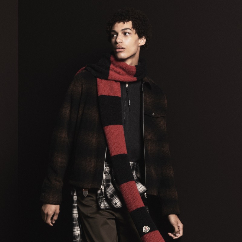 Outerwear Moncler pour homme. Surchemise à carreaux marron, écharpe à rayures rouges et noires, sweat foncé, pantalon marron.