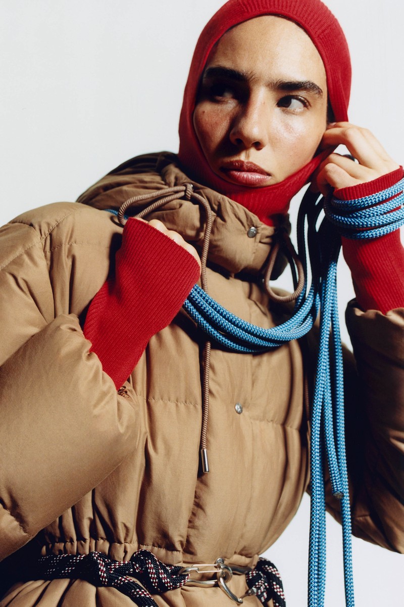 Moncler Re/Icons 2026, Himalaya. Daunenjacke in Camel und rote Sturmhaube, blaues Kletterseil.